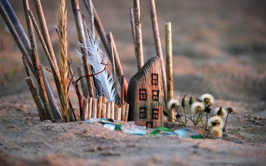 An image of a beach and a small sculpture of a building made out of driftwood.